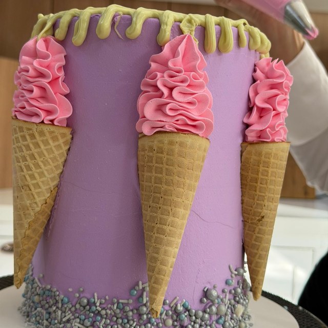 Close em bolo roxo decorado com chantilly rosa e cones