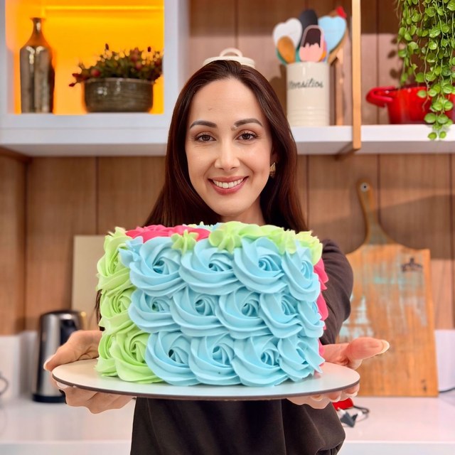 Confeiteira segurando bolo decorado com chantilly azul e verde