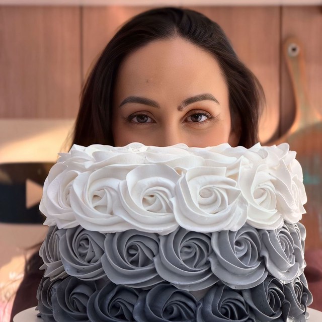 Bolo decorado com rosetas brancas e cinza segurado por confeiteira
